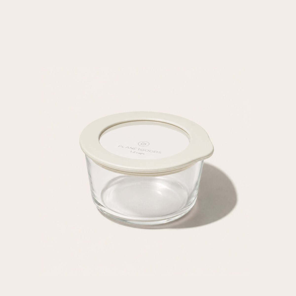 PlanetGoods round borosilicate glass storage container sealed with its lid - a clear glass window set into a cream silicone rim - on a pale background