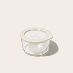 PlanetGoods round borosilicate glass storage container sealed with its lid - a clear glass window set into a cream silicone rim - on a pale background