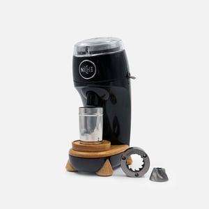 Niche Zero single-dose coffee grinder in black on its oak stand, with the stainless grind cup in place and the conical burrs laid out beside it