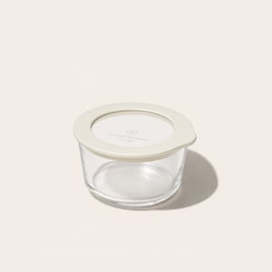 PlanetGoods round borosilicate glass storage container sealed with its lid - a clear glass window set into a cream silicone rim - on a pale background